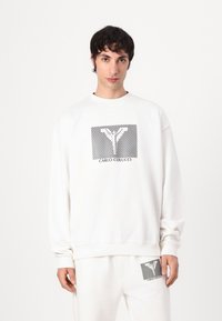 Hvid sweatshirt med et sort og hvidt grafisk design med vandrette striber og tekst "CARLO COLUCCI." Blød, afslappet pasform.