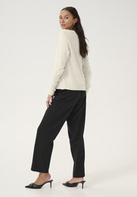 Svetlo bež pulover, sproščen kroj, okrogli izrez, rebrasti manšeti. V kombinaciji z črnimi širokimi hlačami in črnimi mule čevlji s okraski.