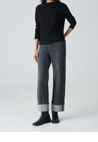 Pull noir texturé associé à un jean gris taille haute à jambes larges, retroussé aux chevilles. Porté avec des bottines noires.