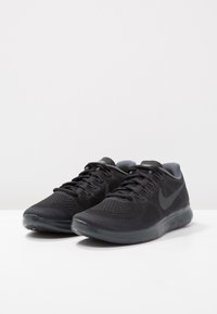 Scarpe sportive nere realizzate in mesh e materiale sintetico, con una superficie testurizzata, lacci e una suola imbottita con un logo sul lato.