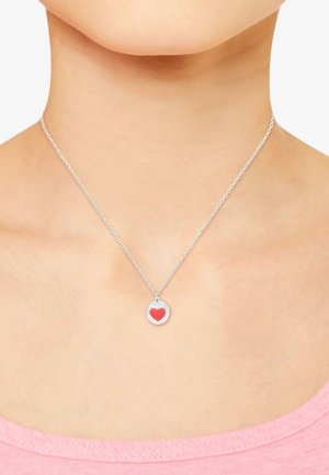 Collana d'argento con un pendente rotondo che presenta un design a forma di cuore rosso, indossata su un collo nudo, in abbinamento a una camicia rosa.