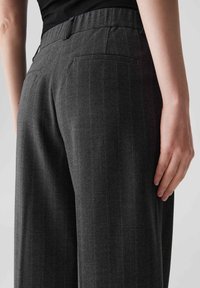 Pantalons en chevron gris avec une taille haute, des poches latérales et une poche arrière, présentant de fines rayures et une texture lisse.