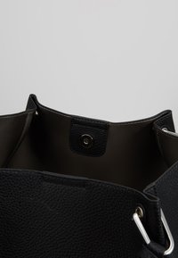 Bolso de mano de cuero negro con textura de grano, parte superior abierta y cierre magnético. Los acentos de hardware plateado realzan el diseño.