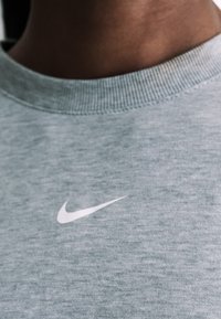 Κοντινό πλάνο ενός ατόμου που φοράει ανοιχτό γκρι μπλούζα με λευκό μικρό λογότυπο Nike swoosh στο στήθος.