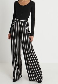 Haut noir à manches longues avec détails de boutons associé à un pantalon taille haute à jambes larges avec des rayures verticales noires et blanches.