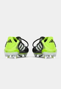 Black and neon green soccer cleats with three silver stripes. Features a textured upper and clear plastic sole with visible metal studs.