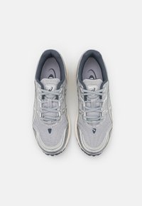 Szare buty sportowe wykonane z siateczki i materiału syntetycznego, charakteryzujące się teksturowaną powierzchnią, sznurowanym fasonem oraz wyściełaną podeszwą.