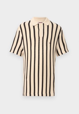 Bež kratka majica s polo ovratnikom s črnimi navpičnimi črtami in majhnim vezenim logotipom na prsih.