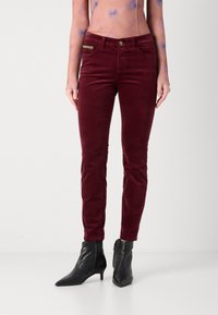 Burgundi spalvos kordūrinės kelnės, pritaikytos slim fit stiliui. Savybės: priekinė kišenė su metaliniais akcentais ir mygtuko užsegimas, derinamos su juodais kulkšnių botais.