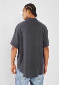 Maglietta a maniche corte grigia scura con tessuto testurizzato, tasca frontale e vestibilità rilassata. Indossata con jeans in denim azzurro chiaro.