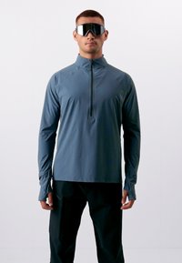 Langarm sporttop in donkerblauw, met een hoge kraag en een kwart-rits. Gemaakt van lichtgewicht, ademend materiaal met duimgaten.