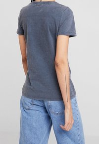 Camiseta gris de algodón de manga corta con cuello redondo, que presenta un ajuste relajado y una textura suave, combinada con jeans de denim azul claro.