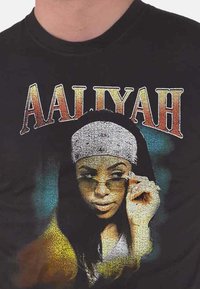 Black cotton t-shirt featuring a graphic of a woman with sunglasses, a silver headband, and “AALIYAH” text above in gradient yellow and red.