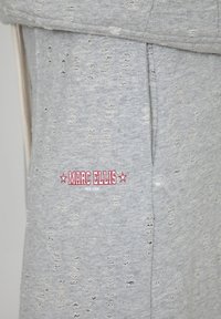Grijze sweatshirt met versleten stof, met een logo in rood en wit, een trekkoordhals en zichtbare stikdetails.