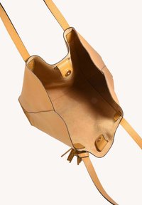 Un sac seau en cuir jaune avec un intérieur doux et non doublé. Il dispose d'une fermeture à pression et de longues sangles plates pour l'épaule.