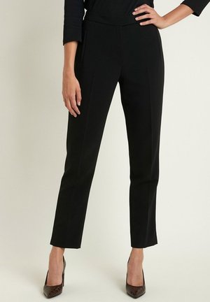 Pantaloni neri su misura con una texture liscia, dotati di una vita aderente, tasche laterali e un design a gamba dritta. Abbinati a tacchi marroni.