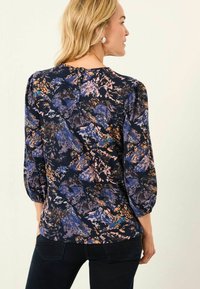 Bunte Bluse mit einem marineblauen Grundton, die ein florales Muster in Pink und Blau aufweist. Dreiviertel-Puffärmel und Knopfdetails auf der Rückseite.
