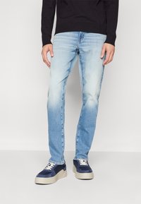 Ljusblå jeans med blekt tvätt, slim fit, bärs med marinblå och krämfärgade plattformssneakers. Svart tröja, ribbade manschetter är synliga.