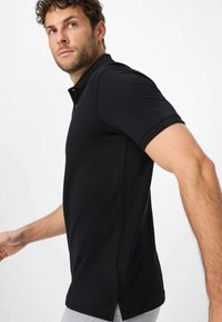Zwarte polo met een klassieke kraag, korte mouwen, knoopsluiting en zijsplitten, gemaakt van een soepele, lichte stof.