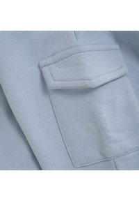 Hellblaues Gewebe mit einer weichen Textur und einer rechteckigen Tasche mit gestickten Akzenten. Die Ansicht konzentriert sich auf das Taschendesign und das Material.