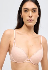 Világos rózsaszín, csipkével szegélyezett, háromszög alakú melltartó, hullámos széllel, vékony állítható pántokkal és geometriai mintával.