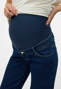 Maternitātes džinsi ar tumši zilu elastīgu paneli komfortam, apvienoti ar klasisku džinsu audumu un standarta piecu kabatu dizainu.