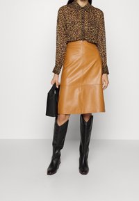 Camicia a fantasia leopardata con bottoni, gonna midi in pelle color nocciola, stivali neri fino al ginocchio e borsa nera. Tessuto liscio, vestibilità sartoriale.