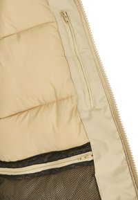 Beige Daunenjacke mit einer glatten Außenschale, einer Innen-Netztasche und kontrastierenden schwarzen Reißverschlussdetails. Das Material wirkt isoliert und weich.