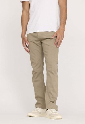 Pantalon en coton beige à coupe droite, avec des détails de couture minimalistes, associé à des baskets blanches et une chemise blanche unie.