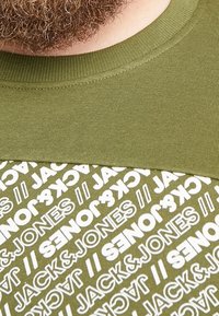 Felpa verde in cotone con un colletto a girocollo testurizzato e un motivo a logo bianco ripetuto. Tessuto morbido con una sezione superiore a contrasto.