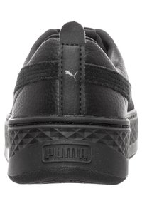 Černé kožené tenisky s texturovaným povrchem, s platformovou podrážkou v diamantovém vzoru a s logem vyraženým na zadní straně.