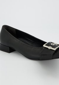 Ballerine plate noire en cuir lisse, avec un bout carré, un petit talon bloc et un détail boucle argentée près de l'avant.