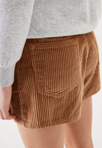 Bruine corduroy shorts met verticale ribbels, voorzien van achterzakken. Het model draagt een lichtgrijs sweatshirt met een aansluitend ontwerp.