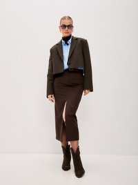 Kratší hnědý blazer, světlá modrá ko�šile, hnědá sukně s bočním rozparkem a hnědé kovbojské boty. Čtvercové sluneční brýle celý outfit doplňují.