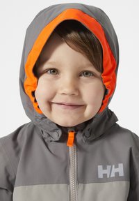 Chaqueta gris con capucha forrada en naranja, que presenta un cierre frontal y un detalle de logo en el pecho. Textura suave, diseñada para calor y comodidad.