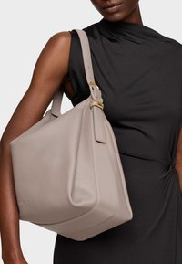 Light beige leather handbag with a textured surface, curved shape, and adjustable strap featuring gold-tone hardware accents.