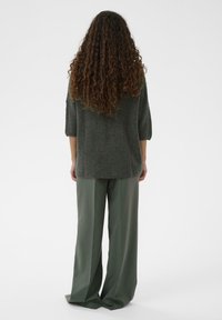 Pulover verde supradimensionat din tricot, cu mâneci trei sferturi, asortat cu pantaloni verzi, cu talie înaltă și pantaloni largi. Material texturat, croială lejeră.
