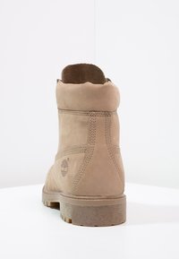 Krémové semišové kotníkové boty s robustní podešví. Má měkký límec a viditelné švy. Logo Timberland na vnější části podpatku.