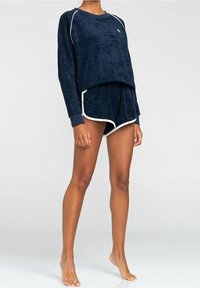 Granatowy zestaw dresowy z weluru, składający się z long sleeve topu z białymi akcentami oraz pasujących szortów z kontrastowym wykończeniem. Miękka faktura przez cały czas.