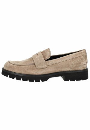 Enkele beige suède loafer met riemdetail en dikke zwarte rubberen zool, gezien van opzij op een witte achtergrond.