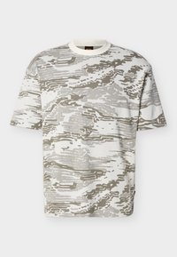 Κοντομάνικο T-shirt με στρογγυλή λαιμόκοψη και αφαίρετο μοτίβο καμουφλάζ σε μπεζ και λευκό, εμφανιζόμενο σε απλό φόντο.