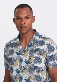 Chemise à manches courtes avec un fond bleu clair orné de motifs tropicaux verts feuillus et bleu marine, confectionnée dans un tissu léger.