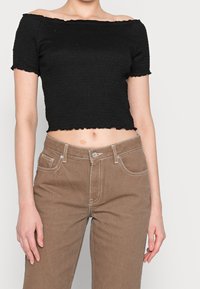 Top negro corto con hombros al descubierto y un acabado texturizado, combinado con pantalones marrones de cintura alta que cuentan con un cierre de botón y costuras en contraste.