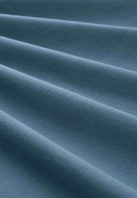 Texturiert blauer Stoff mit einer glatten Oberfläche, der Falten und Knicke zeigt. Licht reflektiert sanft und betont ein gewebtes Muster und den Glanz.