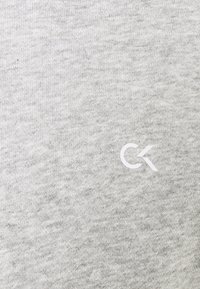 Lichtgrijs katoenen t-shirt met een klein wit CK-logo. De stof lijkt zacht met een subtiele textuur en heeft geen zichtbare patronen.