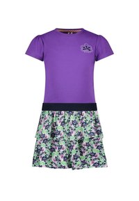 Fioletowa bluzka z krótkim rękawem i marszczonymi bufkami, w połączeniu z falbaniastego spódnicą w kwiatowy wzór z zielonymi, fioletowymi i niebieskimi akcentami.