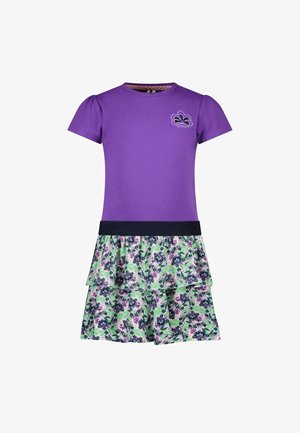 Fioletowa bluzka z krótkim rękawem i marszczonymi bufkami, w połączeniu z falbaniastego spódnicą w kwiatowy wzór z zielonymi, fioletowymi i niebieskimi akcentami.