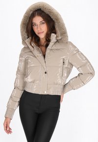 Geacă matlasată bej, lucioasă, cu croial�ă scurtă și glugă căptușită cu blană. Are buzunare laterale cu fermoar și manșete striate. Suprafață texturată cu finisaj lucios.