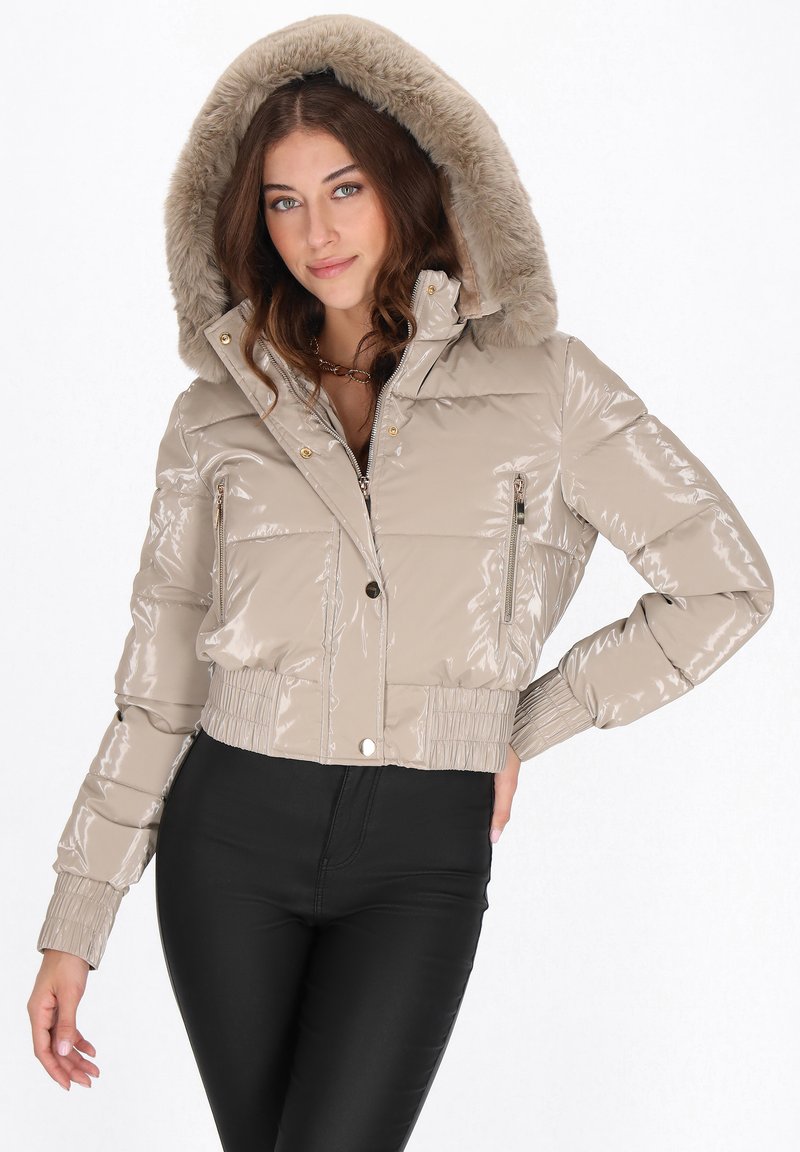 Geacă matlasată bej, lucioasă, cu croială scurtă și glugă căptușită cu blană. Are buzunare laterale cu fermoar și manșete striate. Suprafață texturată cu finisaj lucios.