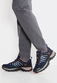 Buty trekkingowe z ciemnoniebieskiego materiału syntetycznego, czarnymi akcentami, jasnymi sznurowadłami oraz teksturowaną podeszwą zapewniającą przyczepność. Lekka konstrukcja.